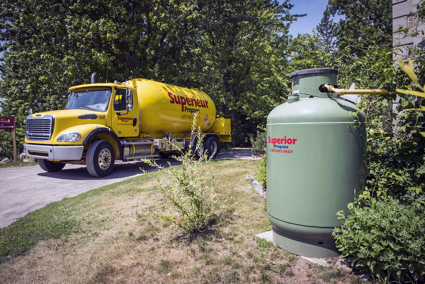 A yellow Superior Propane truck is parked on the side of a road with a green 420lb propane tank is in the foreground.