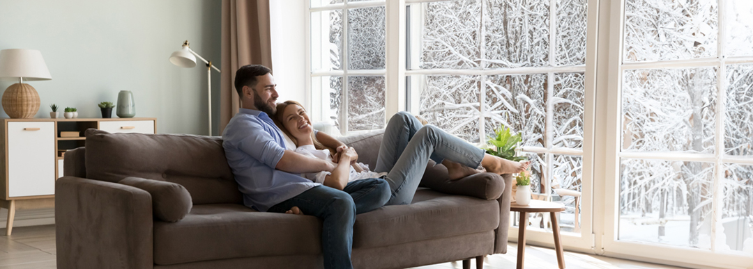 man and woman sitting in living room looking at the snow outside