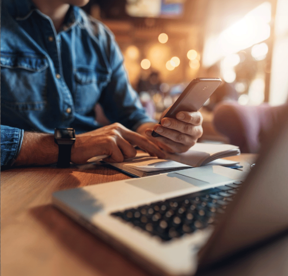 close up of man holding cellphone in front of laptop