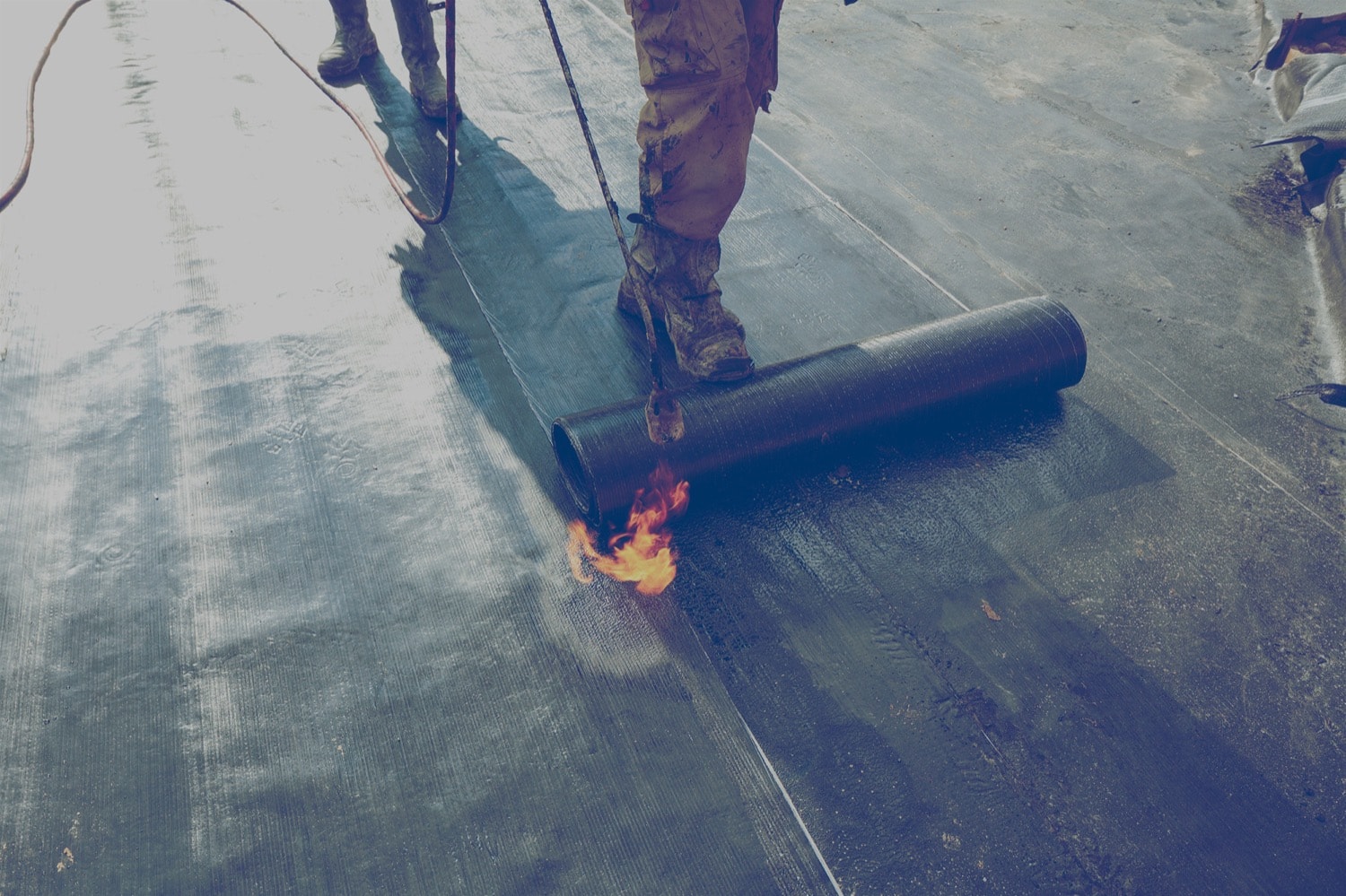Construction worker using a hand-held propane torch to heat bitumen to create a waterproof seal on a roof. 