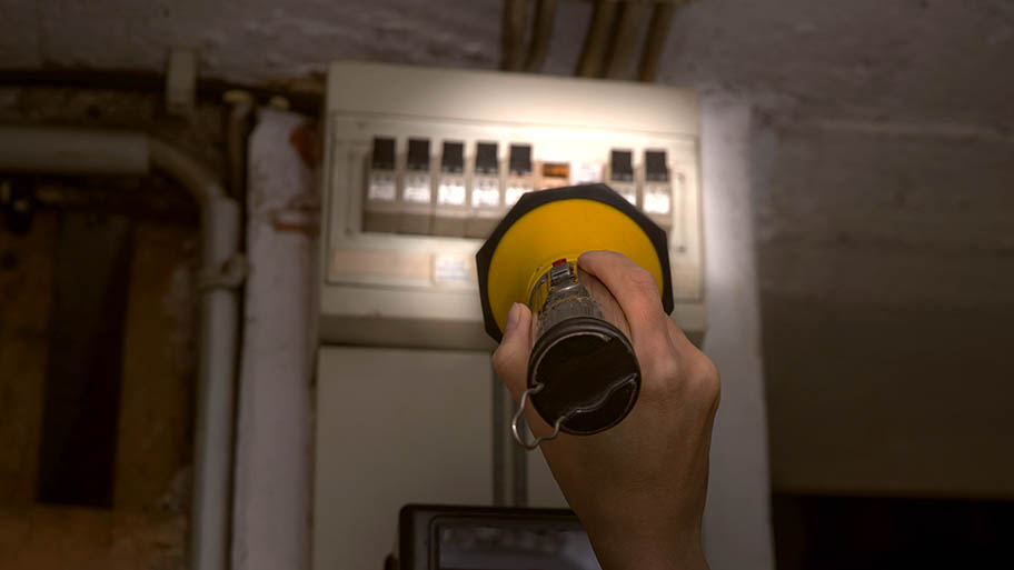 Person holding a flashlight to illuminate a circuit breaker in a basement. 