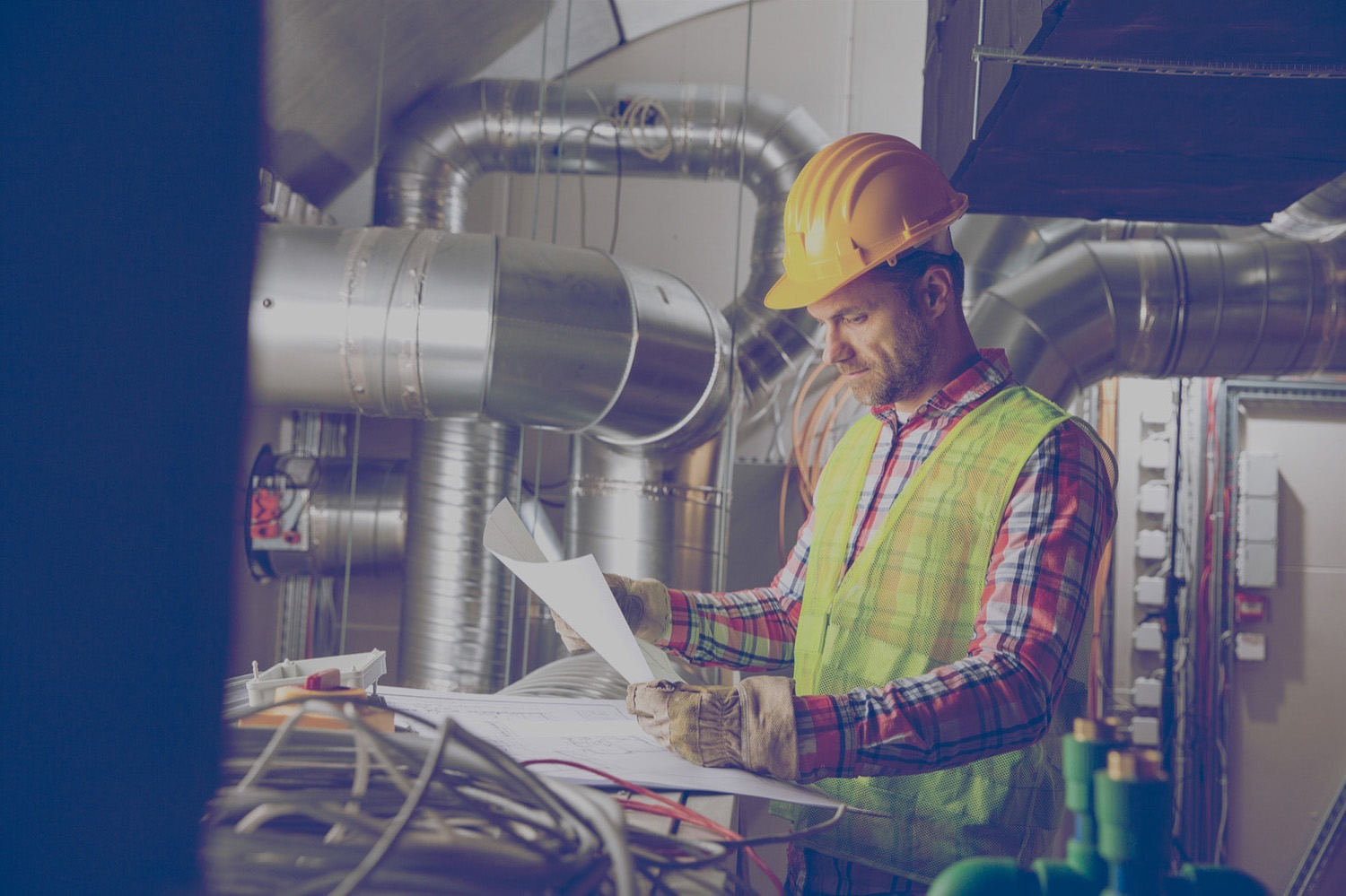 Construction worker looking at blueprints in an industrial furnace room that uses propane. 