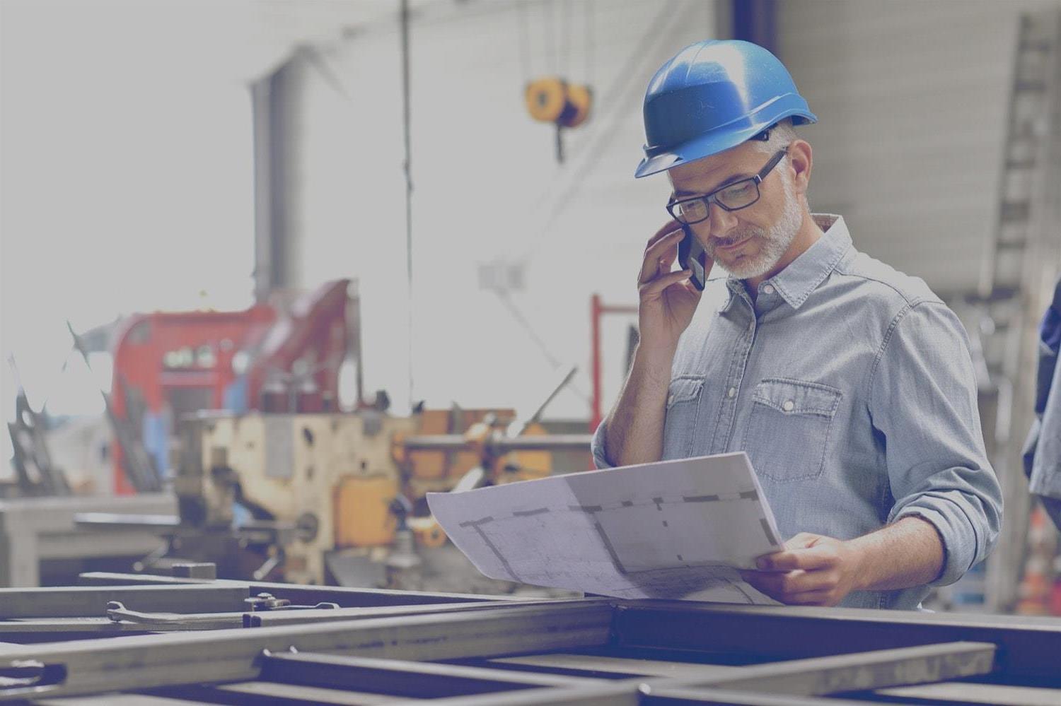 Safety inspector at a propane powered construction site looking at a blueprint and talking on a cell phone. 