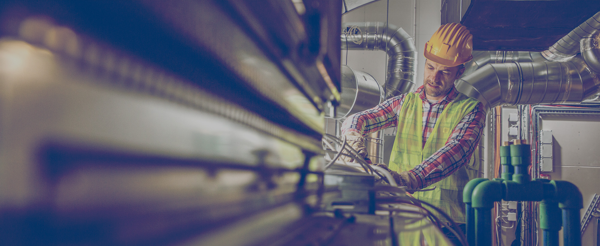 Construction worker making an adjustment to equipment in a large industrial furnace room that uses propane heating. 