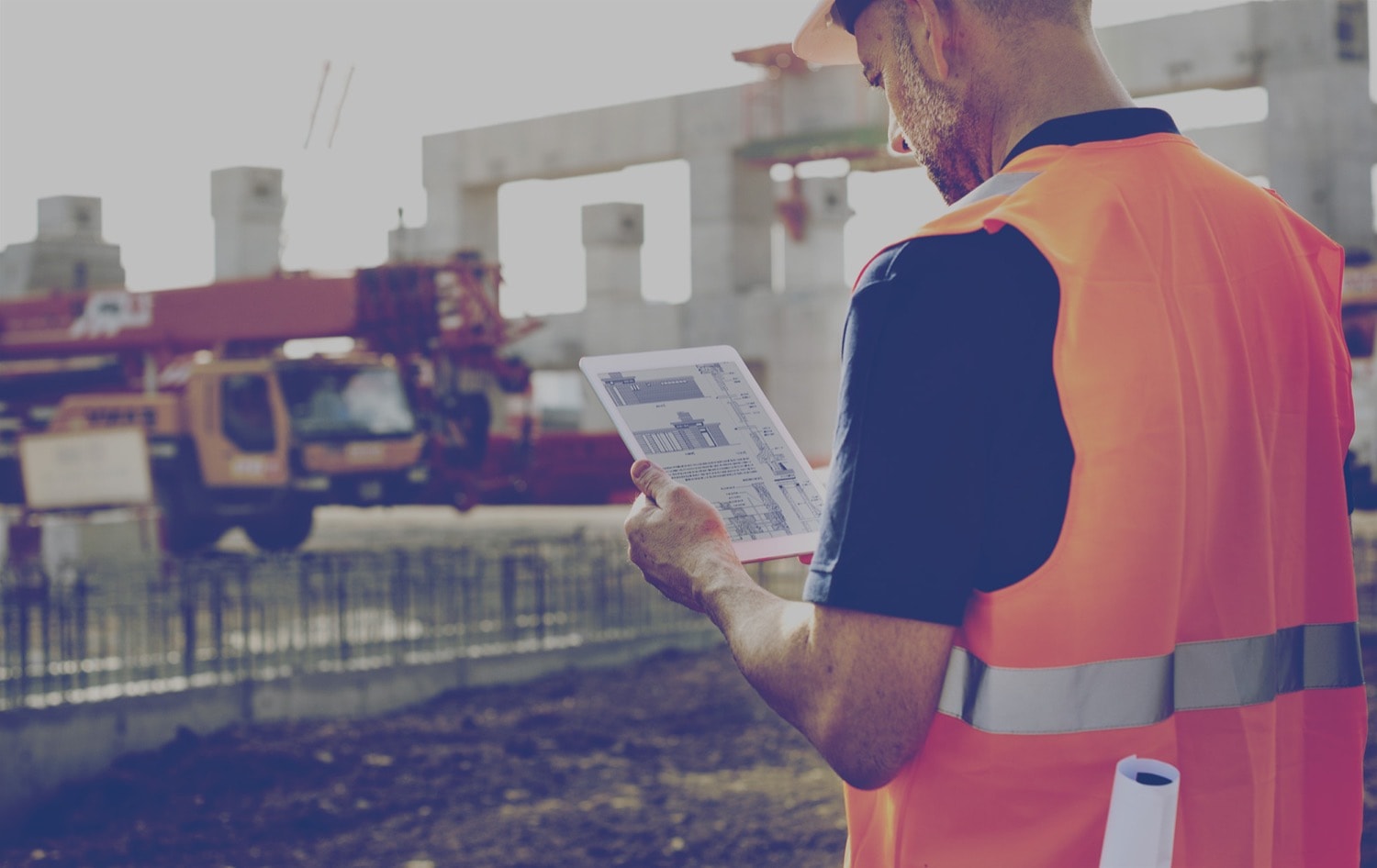 A construction worker on a job site looking at blueprints on a tablet. 