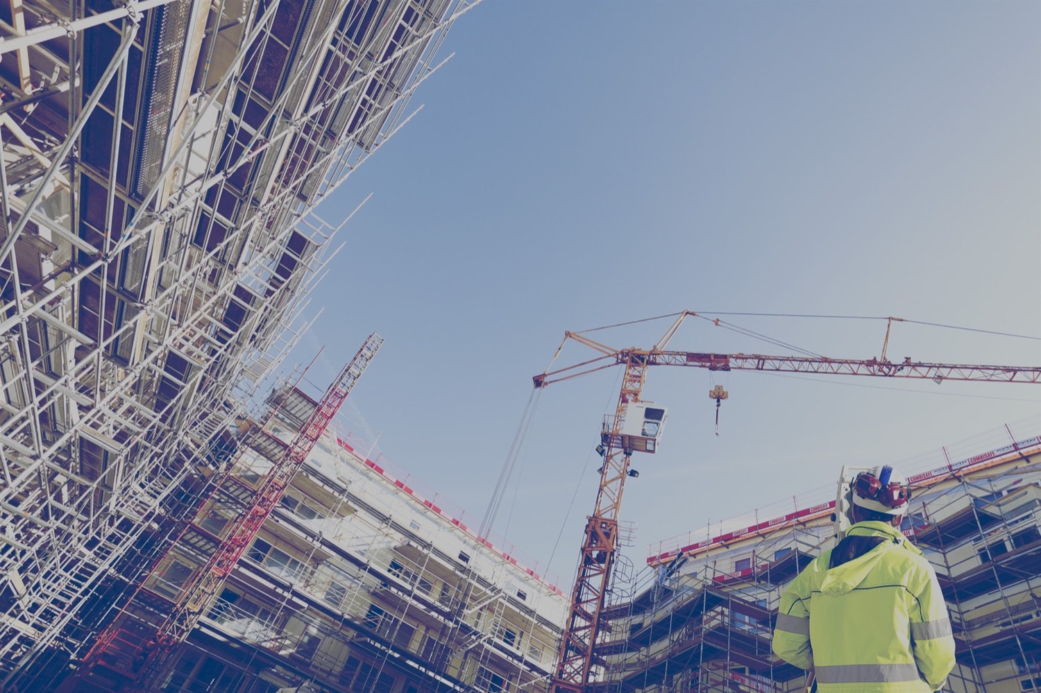 Construction worker looking up at a crane and a High Rise building being constructed. 