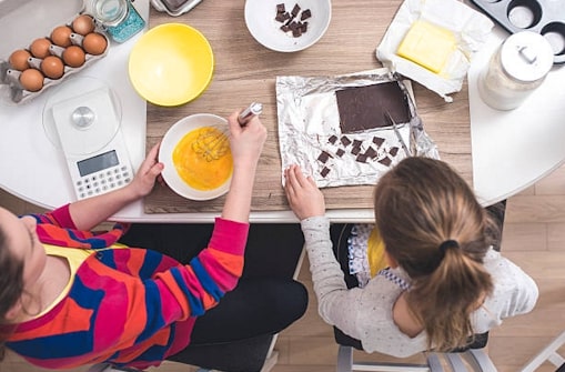 Mother and daughter sitting at kitchen table preparing baked goods. 