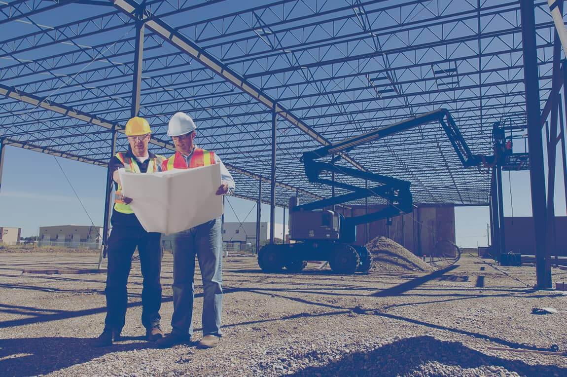 Two construction workers looking at a blueprint on the job site for a commercial building.