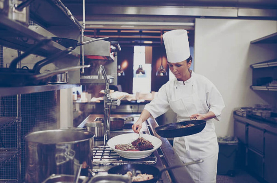 Chef transferring food from a skillet on a propane stove in a commercial kitchen. 