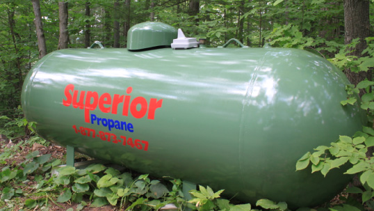 Green Superior Propane tank in a forest.