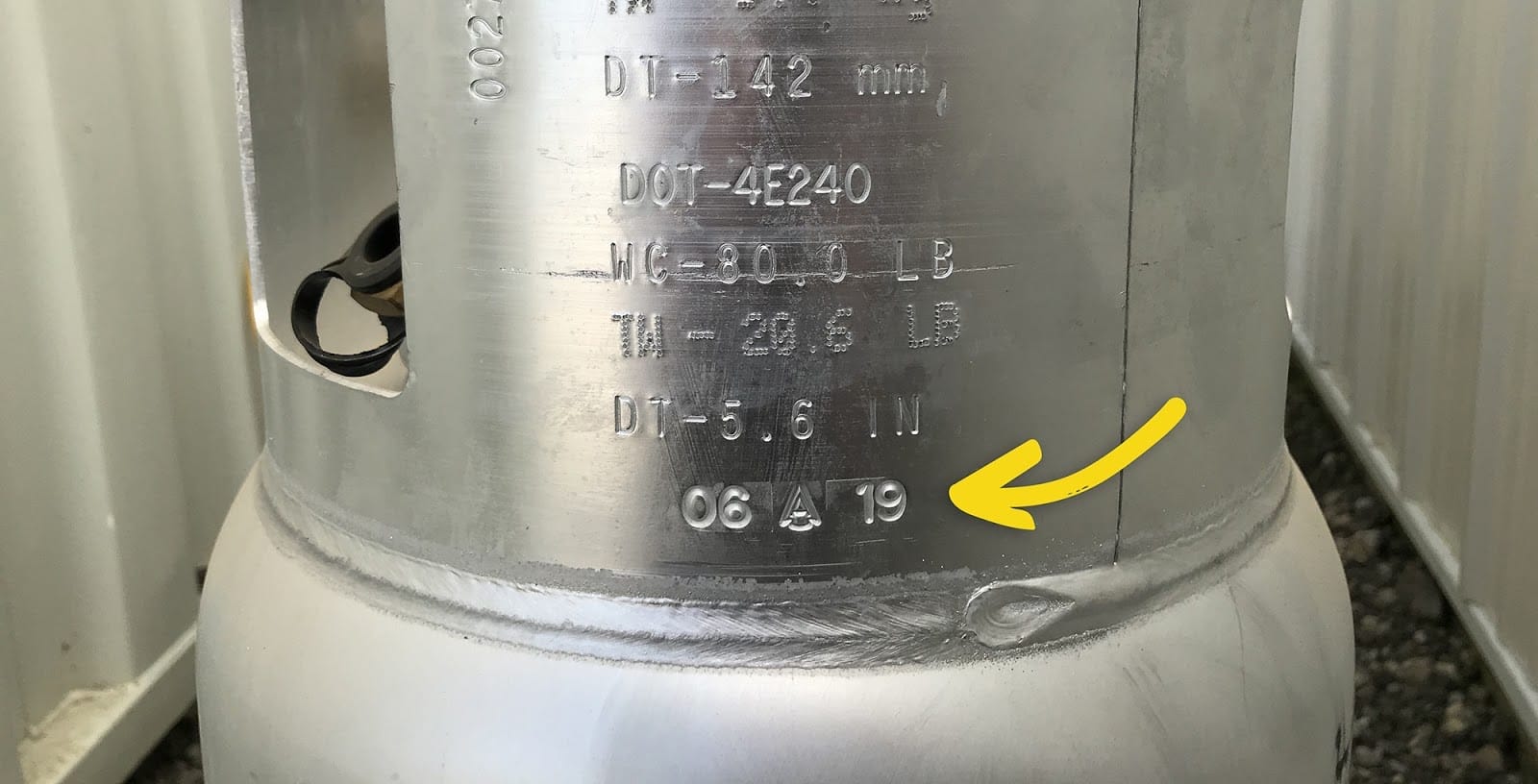 Closeup of a propane tank collar with an arrow pointing to the manufacturer’s date stamp.