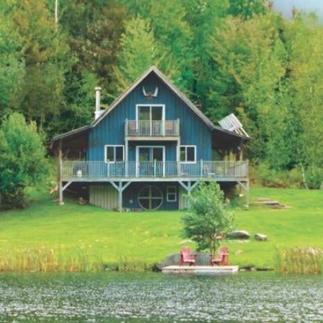 Blue cottage on a lake in a rural, forested location. 