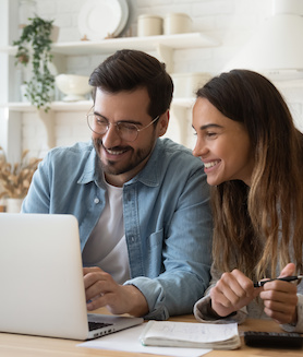 A happy young couple using a laptop to plan their monthly budget
