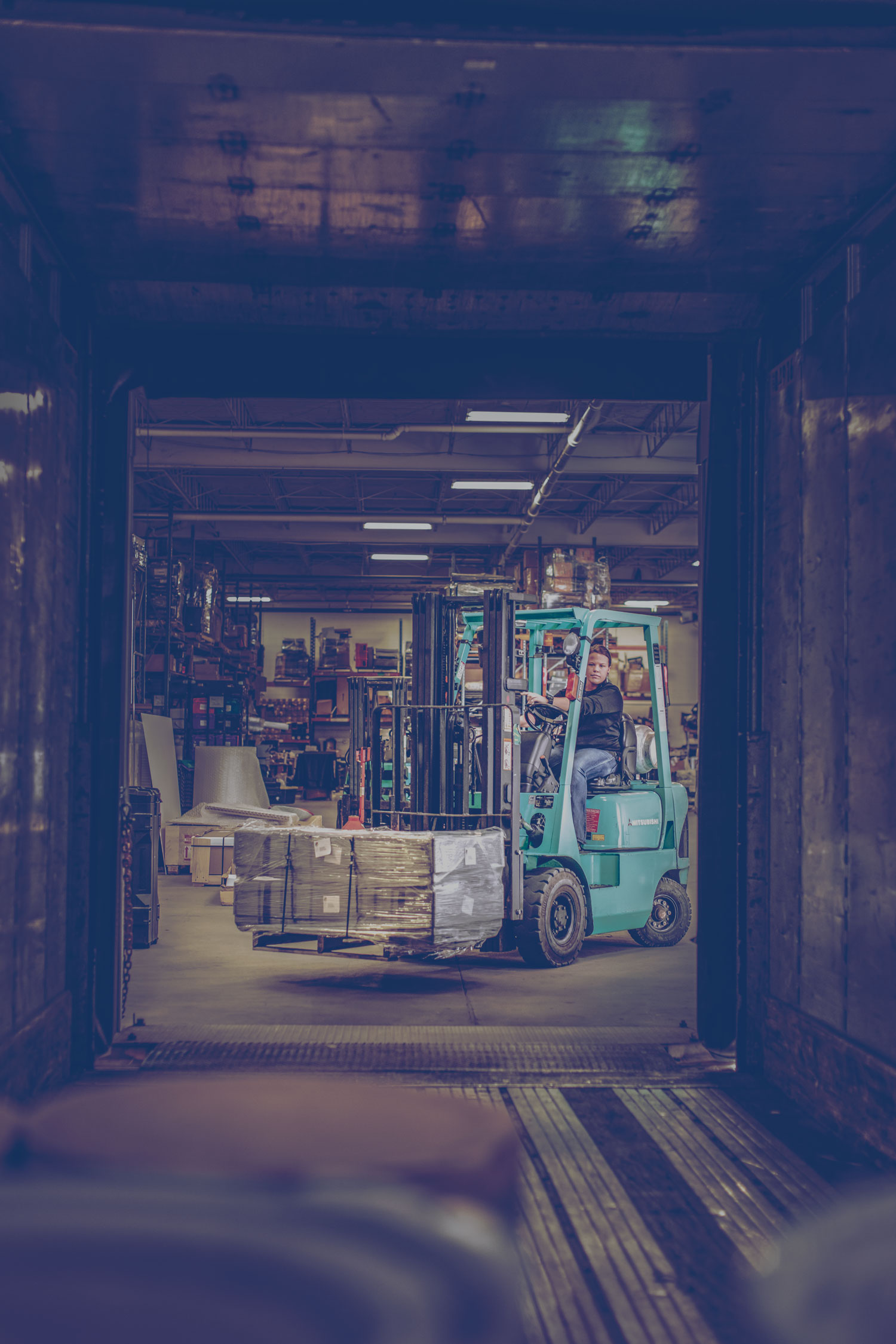 A propane-powered forklift in a warehouse filling a trailer with a pallet of goods.