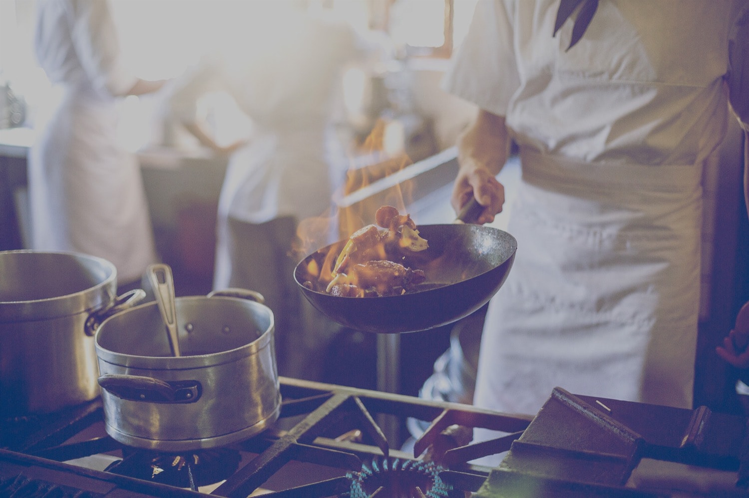 A chef is tossing meat in a frying pan. There is a flame coming from the pan. 