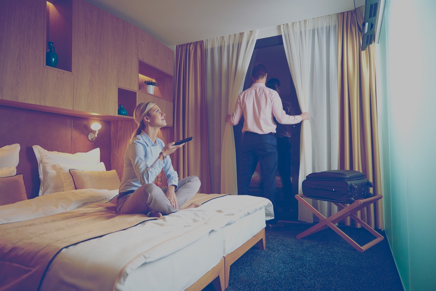 Couple in a hotel room. The woman is turning on a propane-powered heater, and the man is looking out the window. 
