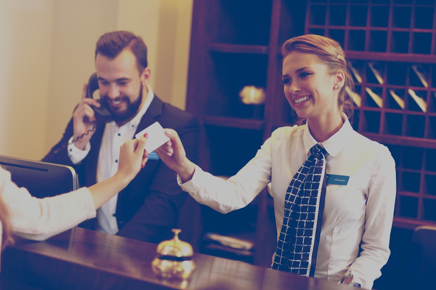 Front desk attendant at a hotel taking a room card while another employee talks on the phone. 