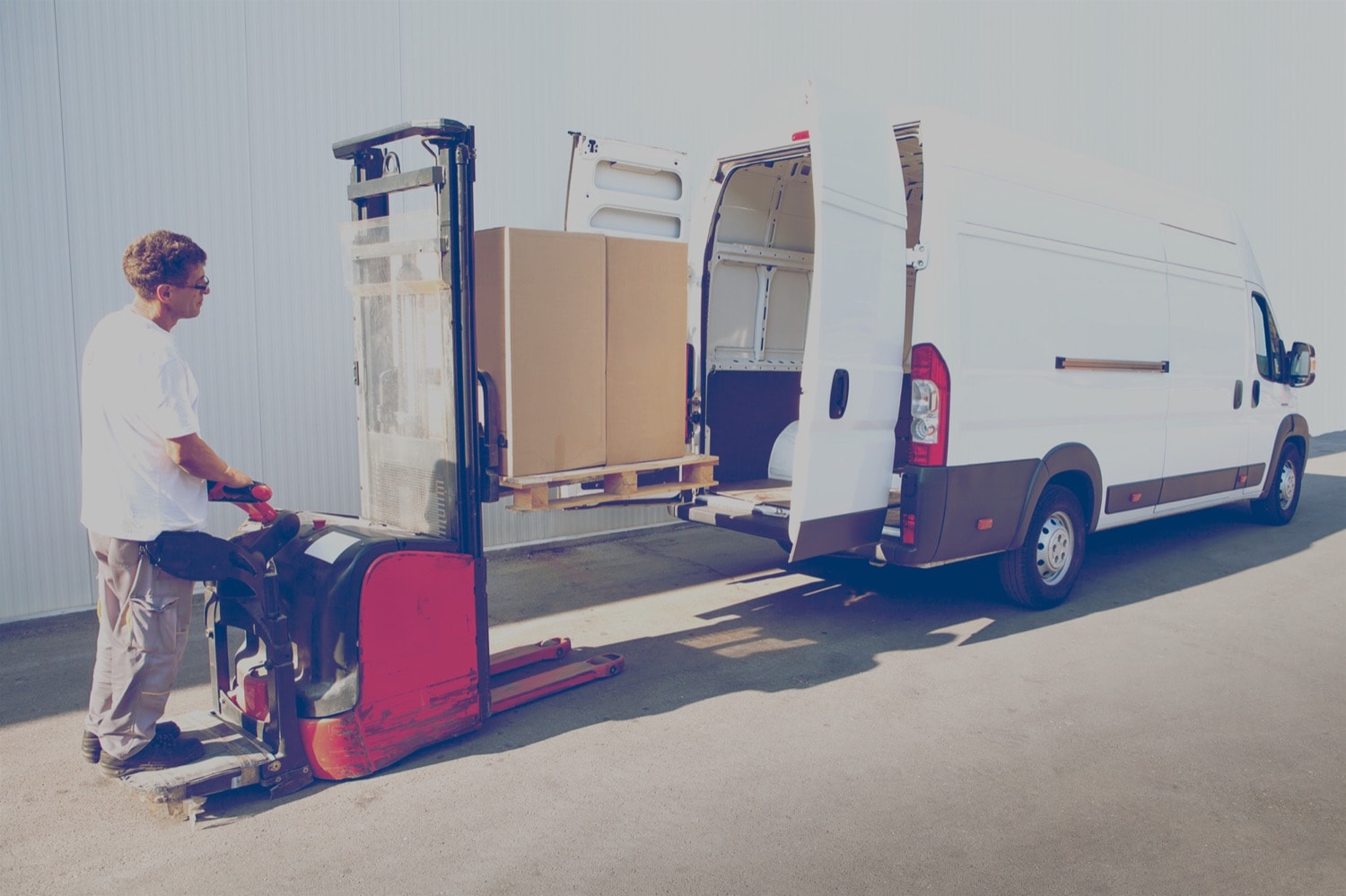 Man placing a skid in the back of a van using a stand up forklift. 