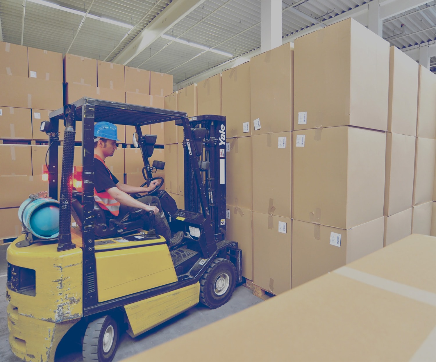 Man driving a propane-powered forklift. He is placing the forks under a skid filled with cardboard boxes. 