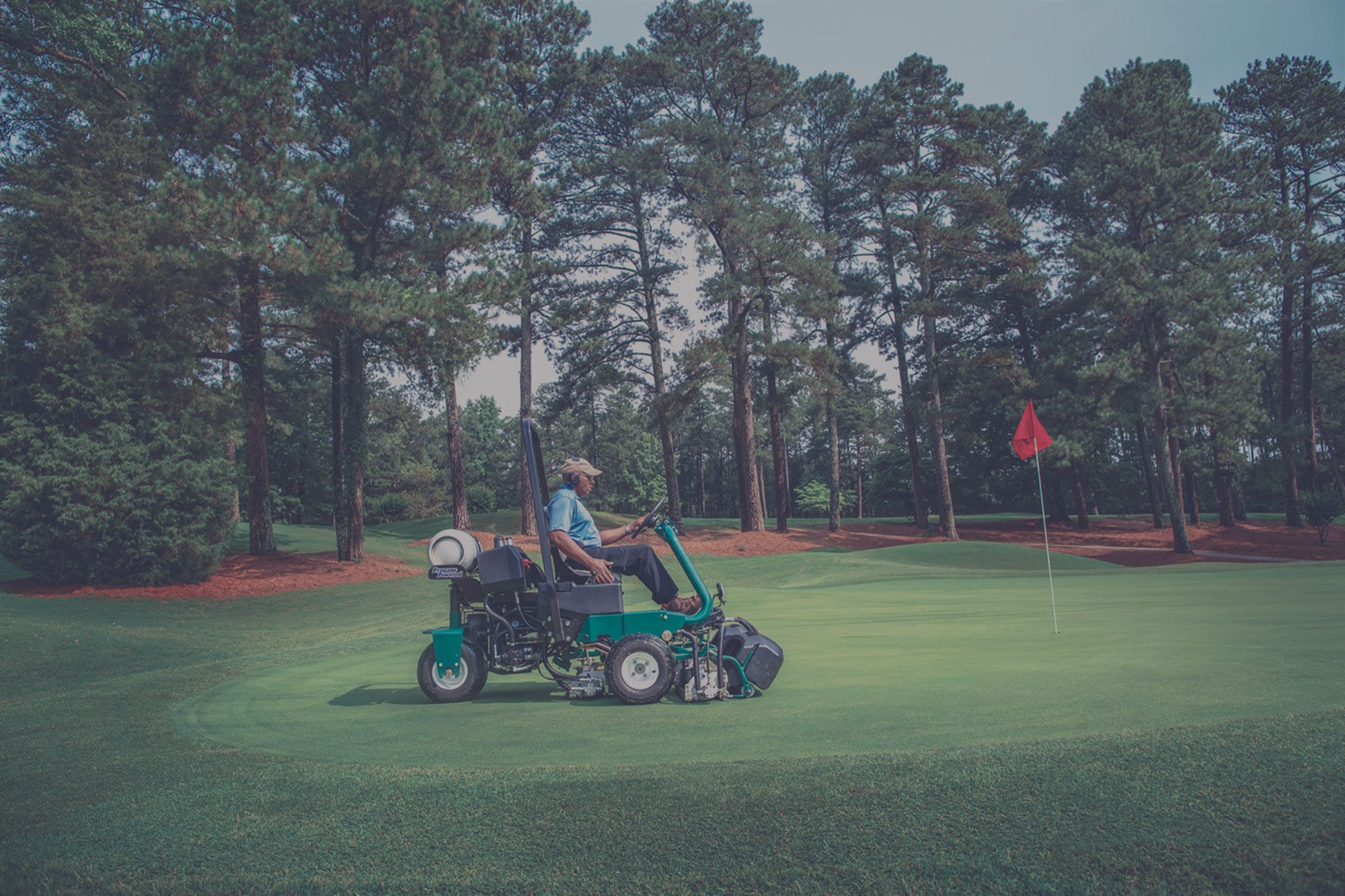 A man driving a propane-powered riding lawn mower at a golf course. 
