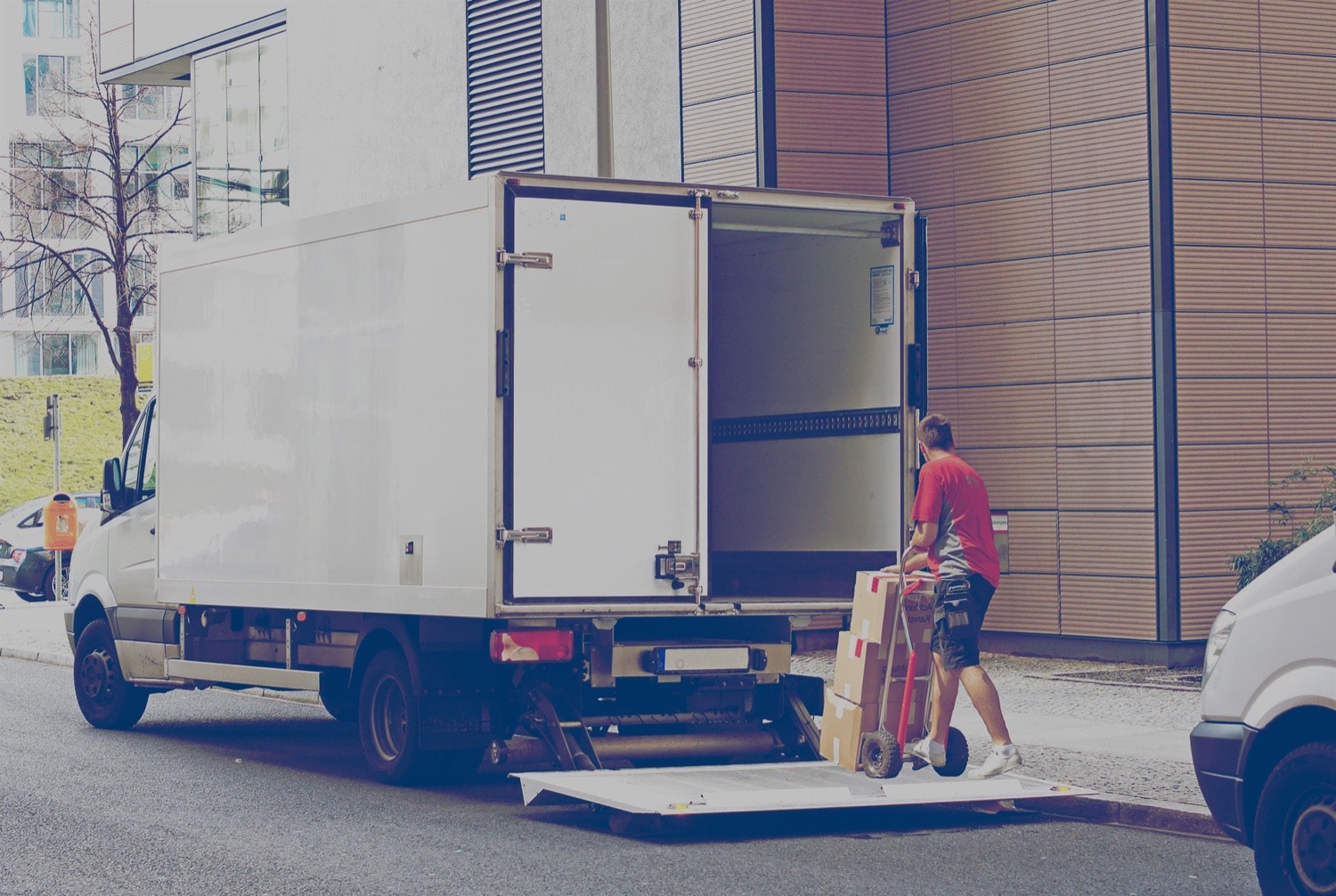 Man using dolly loading boxes into the back of a moving van parked in an urban area.