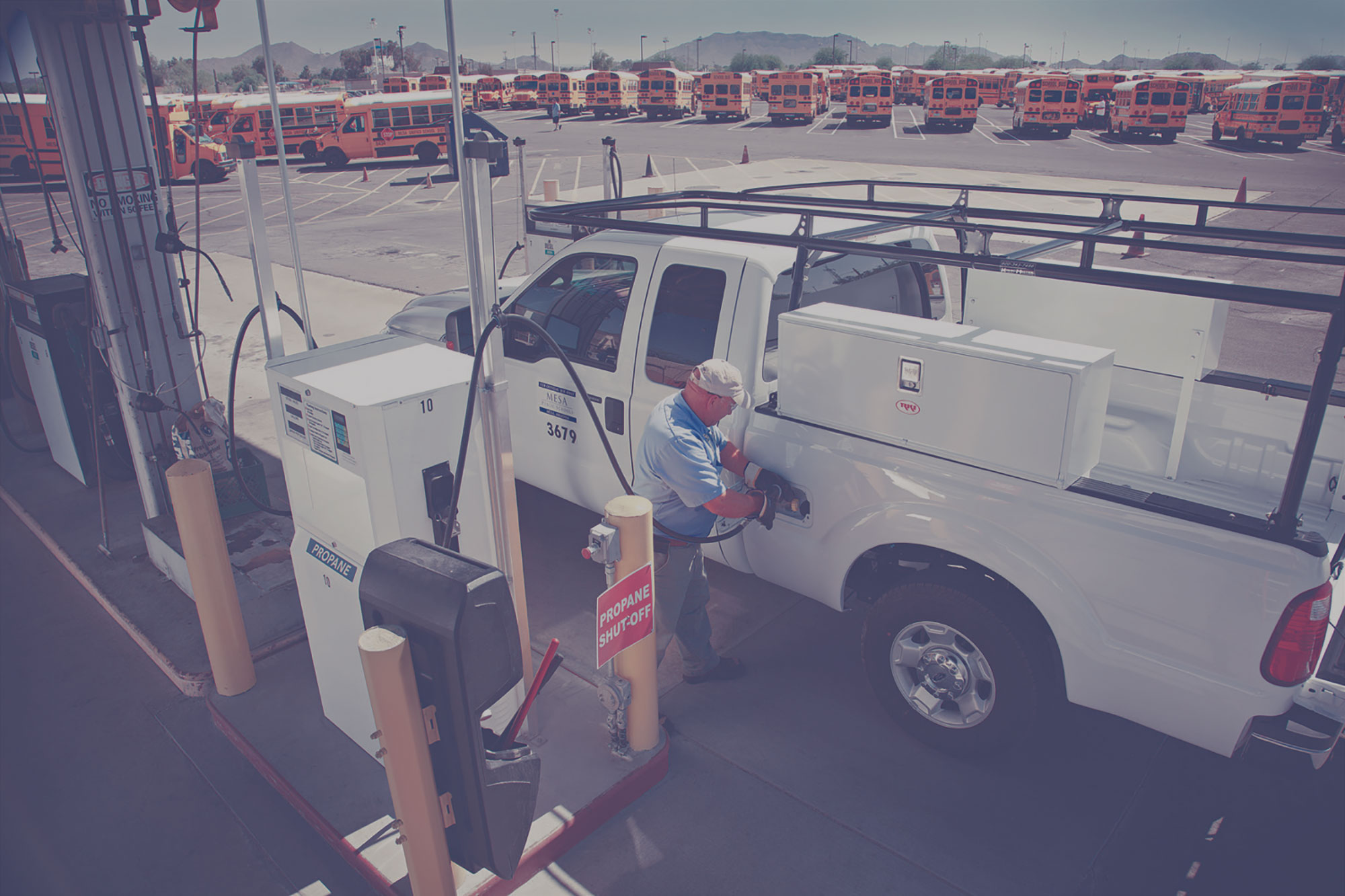 Man filling a pickup truck with propane autogas at a card lock station. There is a fleet of school buses in the background.