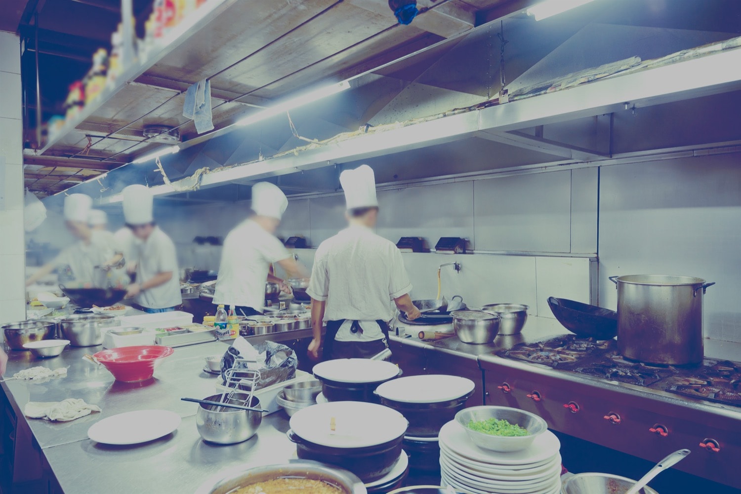 Multiple cooks working in a large restaurant kitchen using propane-powered ranges and ovens. 