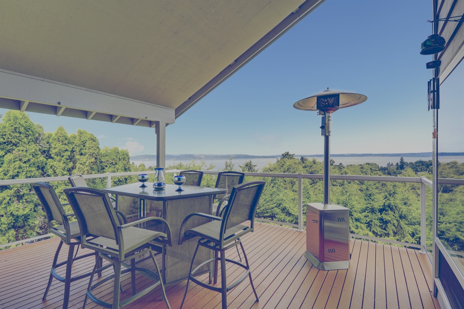 Deck with table and propane heater overlooking a forest, lake, and mountains. 