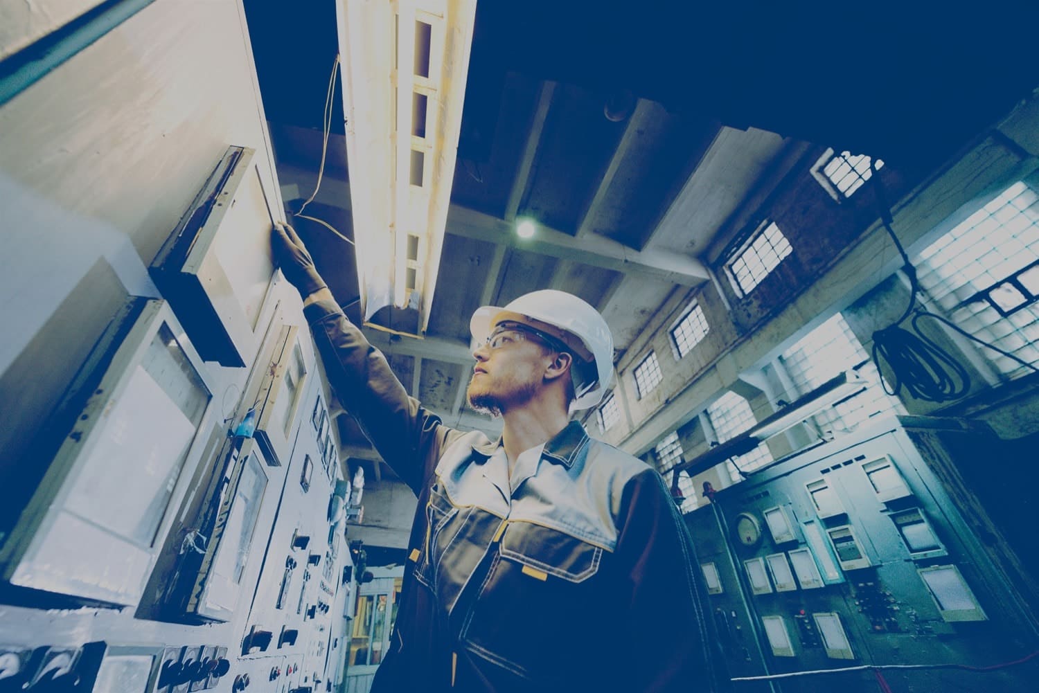 A male worker in a white hard hat checking electronic equipment in a large building