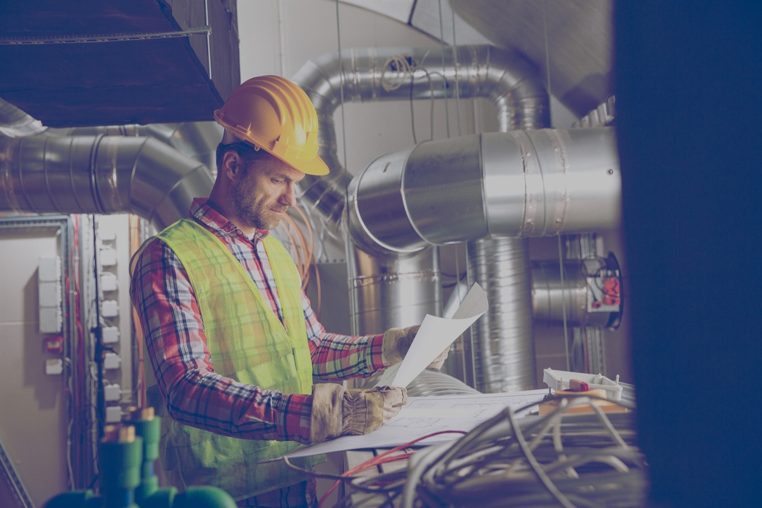 Construction worker reviewing blueprints in a industrial furnace room.