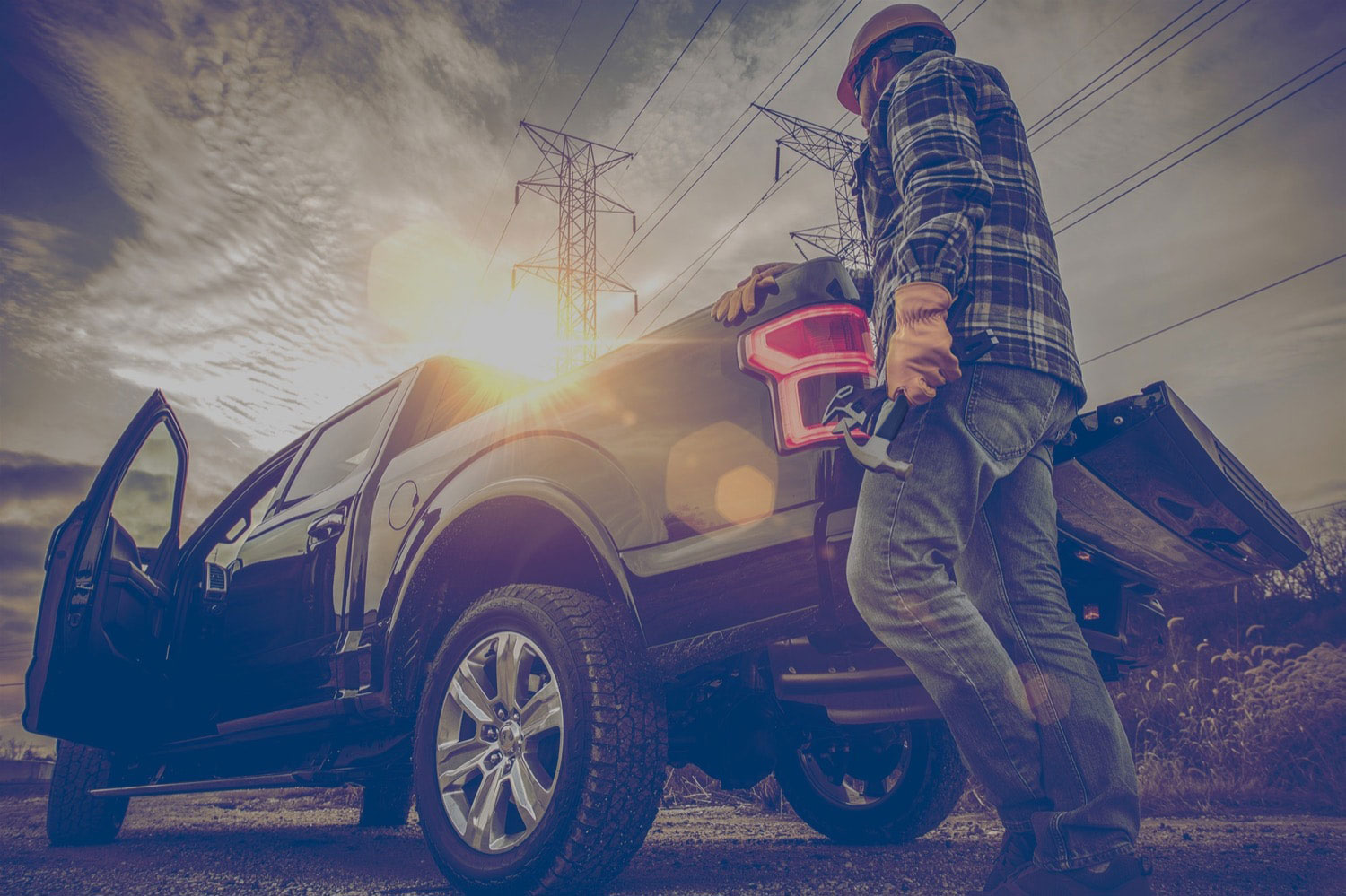 Construction worker holding tools standing at the tailgate of a black pickup truck that uses propane autogas. 