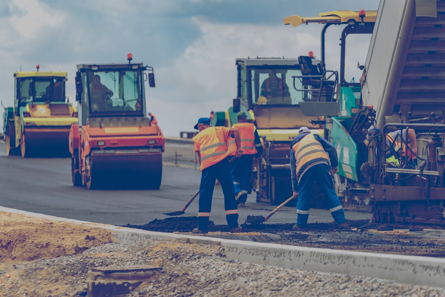 Crew spreading asphalt on a road as steamrollers smooth it out. 