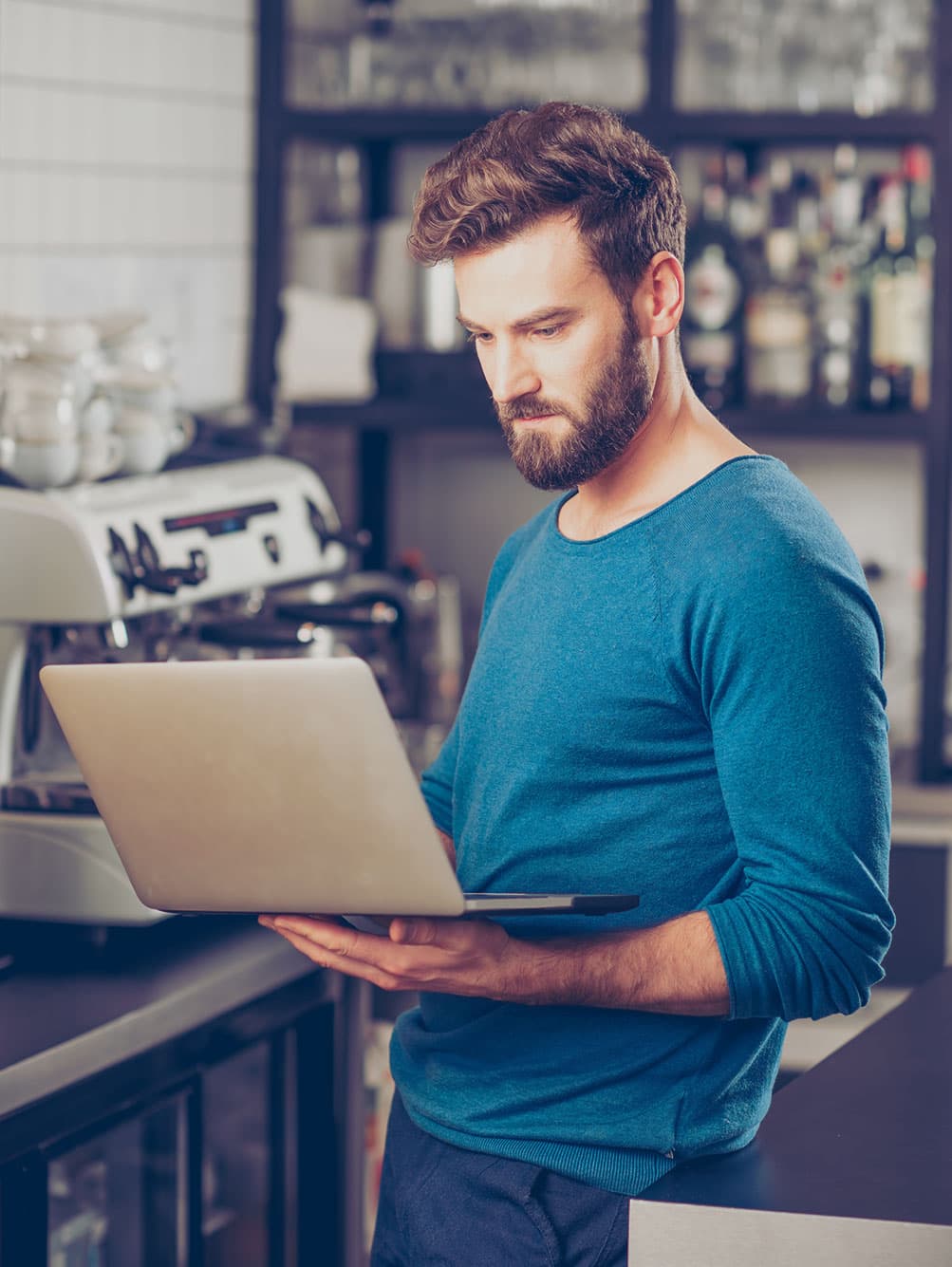 Barista looking at a laptop near espresso machine.