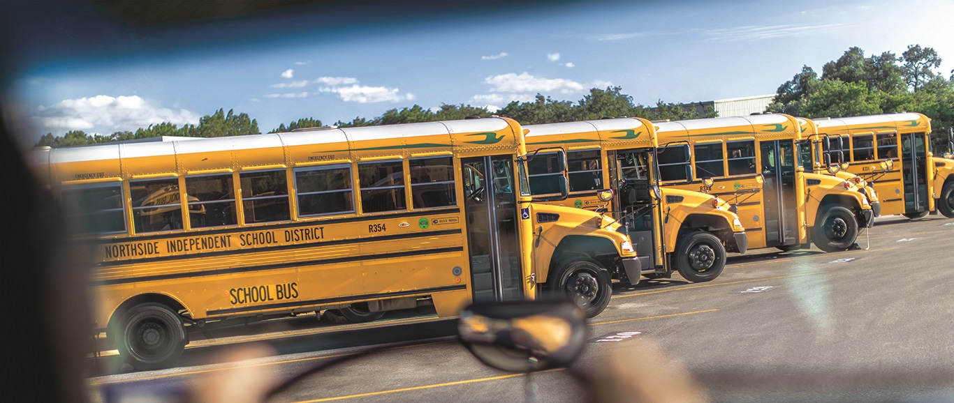 Photo taken over the shoulder of a bus driver driving with propane school buses in front of him