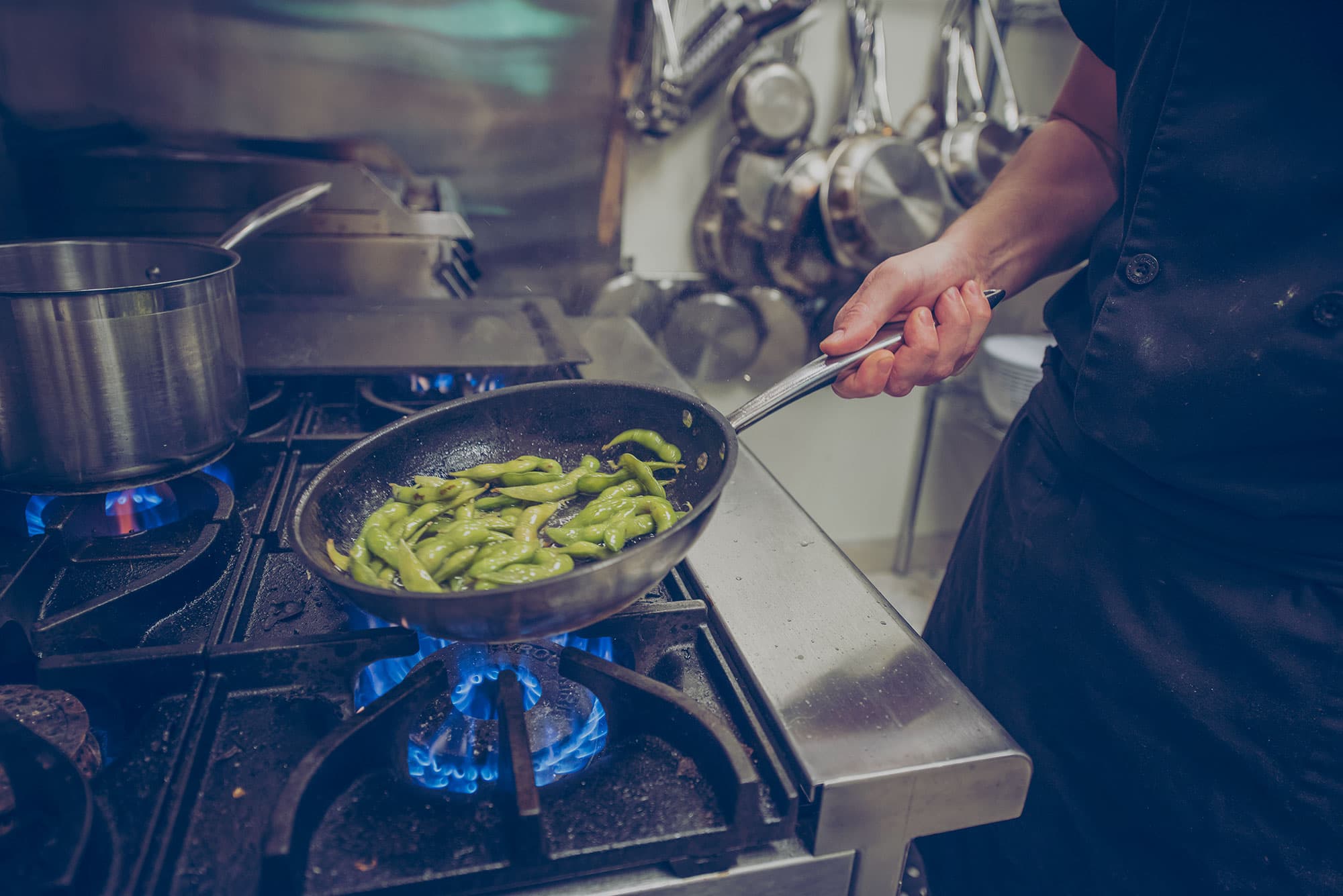 Chef cooking edamame in a pan using a propane range. 