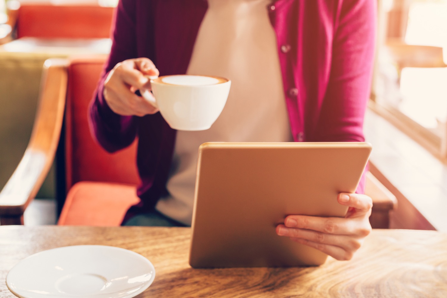 Woman holding a latte while looking at a tablet in a cafe. 