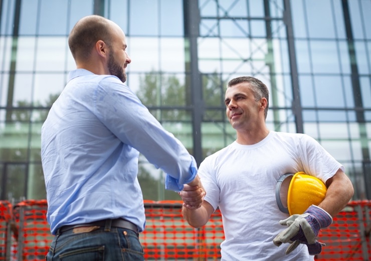 Construction workers shaking hands outside of an office building. 