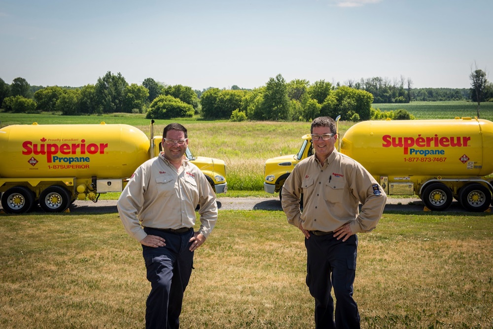 Two Superior Propane employees standing in front on their trucks on a sunny day.