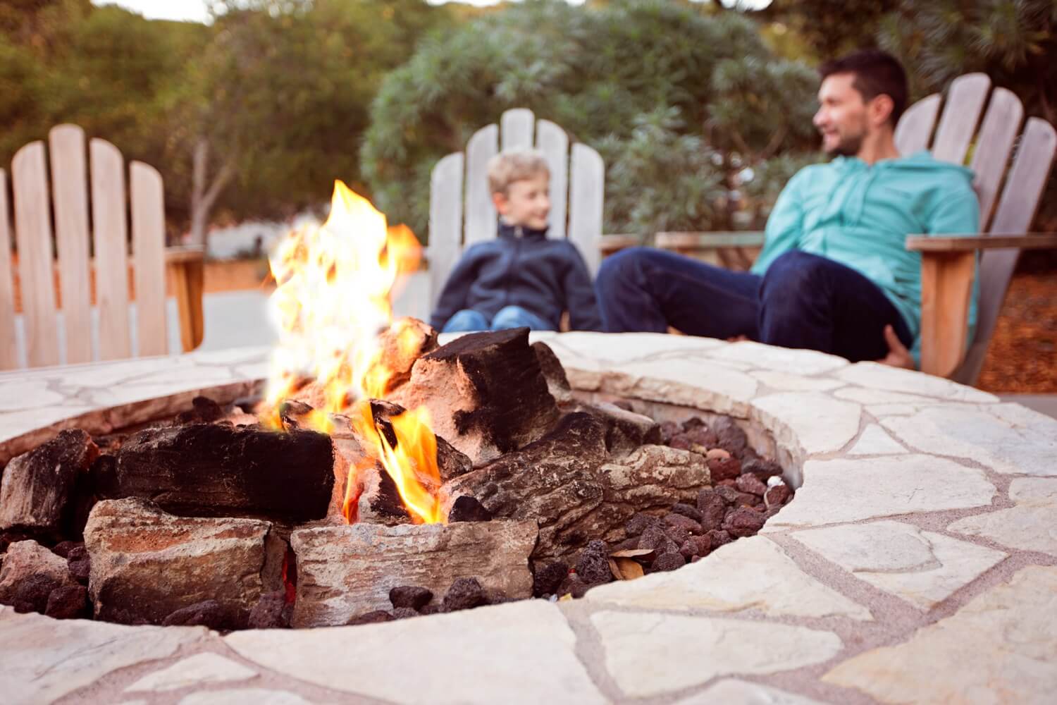 Father and son sitting outside next to propane-powered fire pit. 
