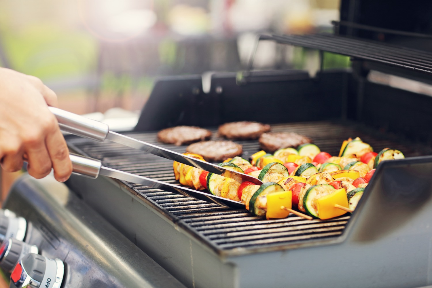 Barbequing vegetable kabobs and burgers on a propane grill. 
