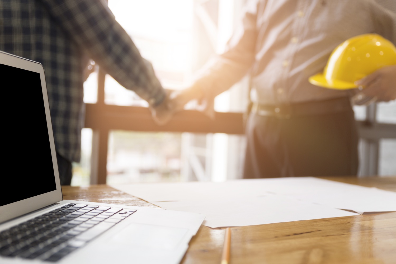 Construction workers shaking hands in front of a laptop. 