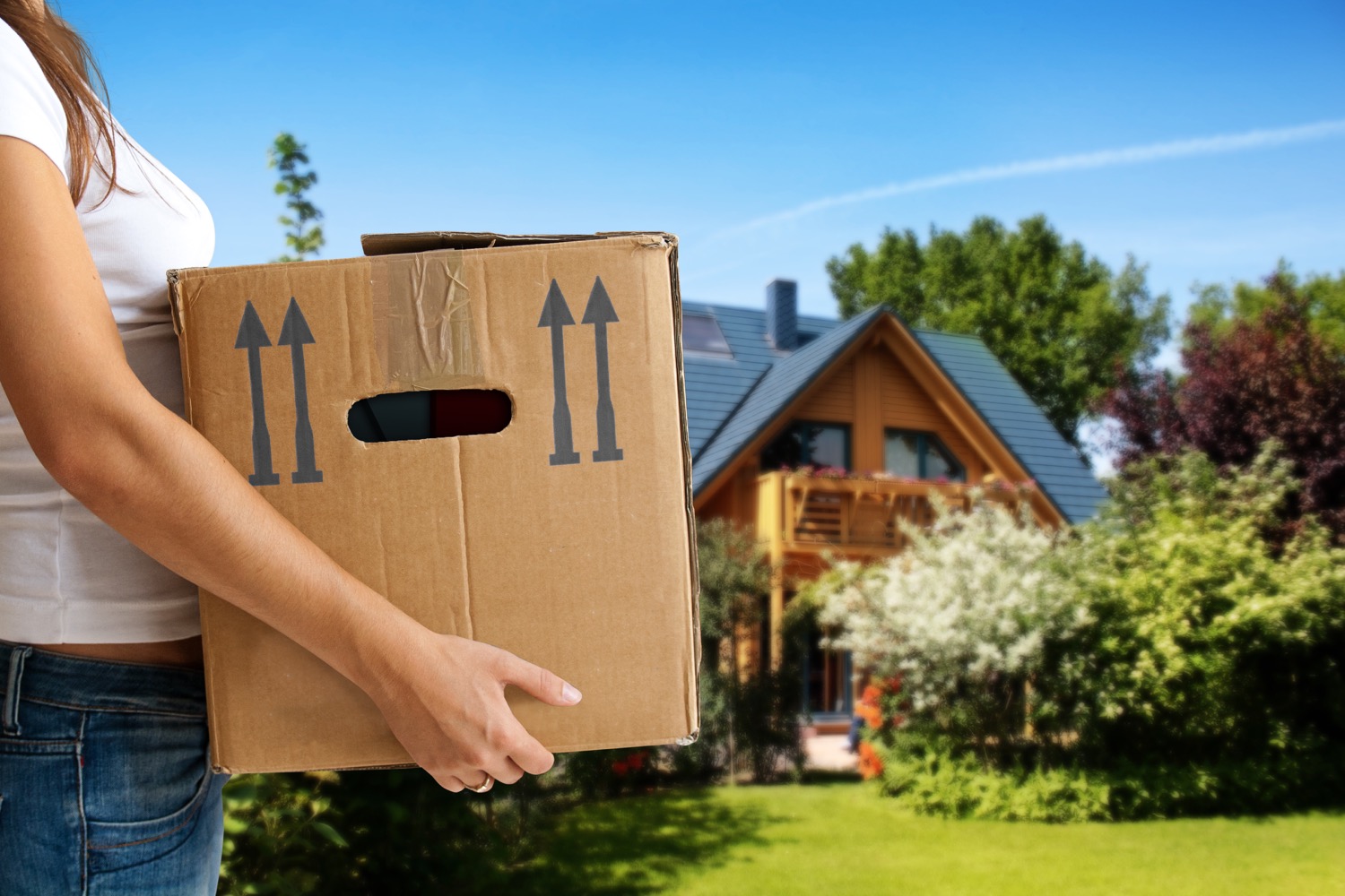 Woman holding a cardboard box in front on a home. 