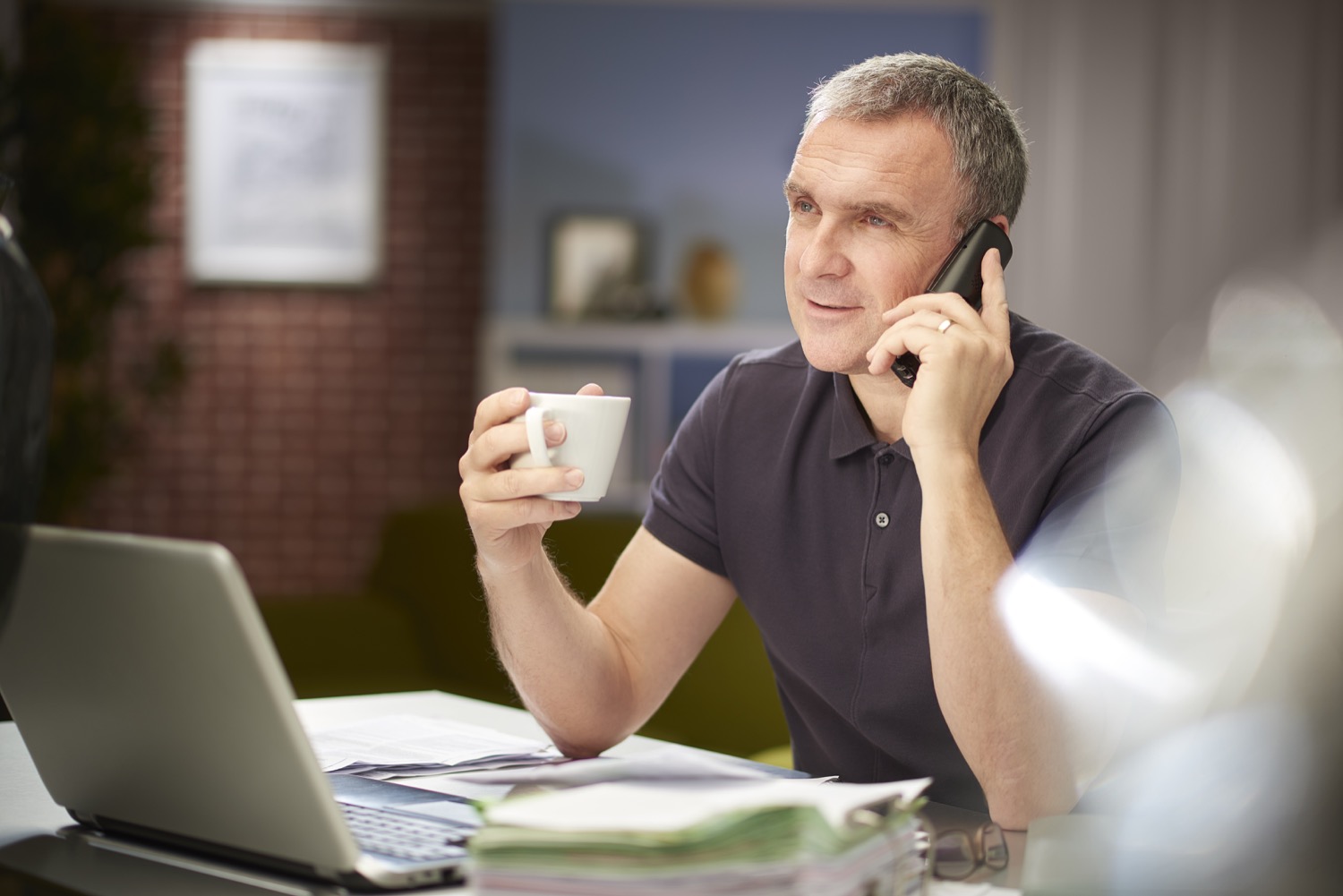 A man sitting in front of a laptop holding a coffee and talking on the phone about Superior Propane pricing plans. 