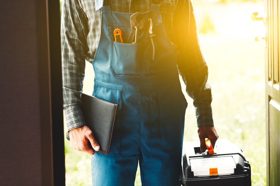 Professional at the front door of a house holding toolbox ready to service a water heater. 