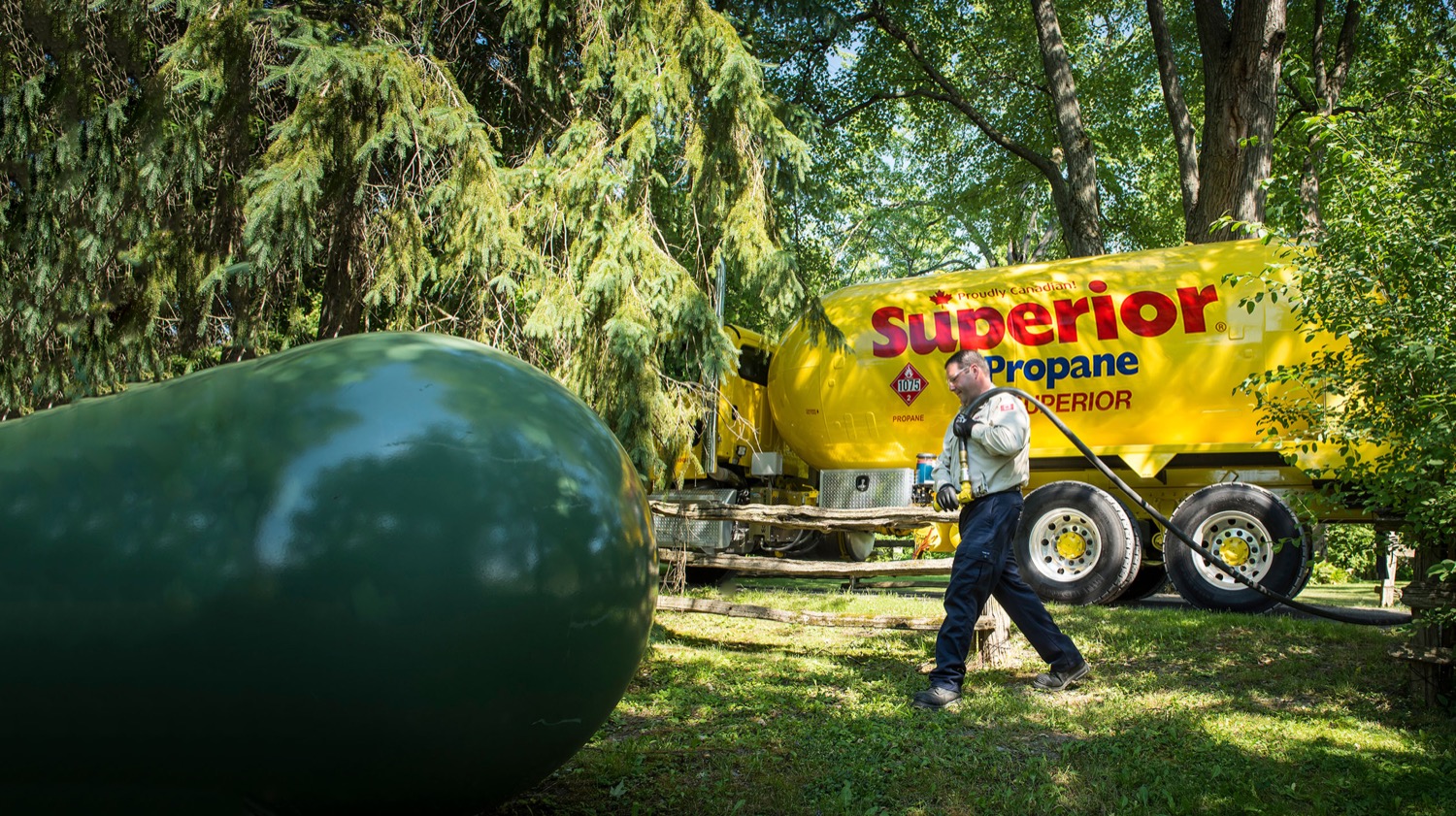 Employé de Supérieur Propane se préparant à remplir un réservoir de propane de couleur verte, dans un secteur boisé.