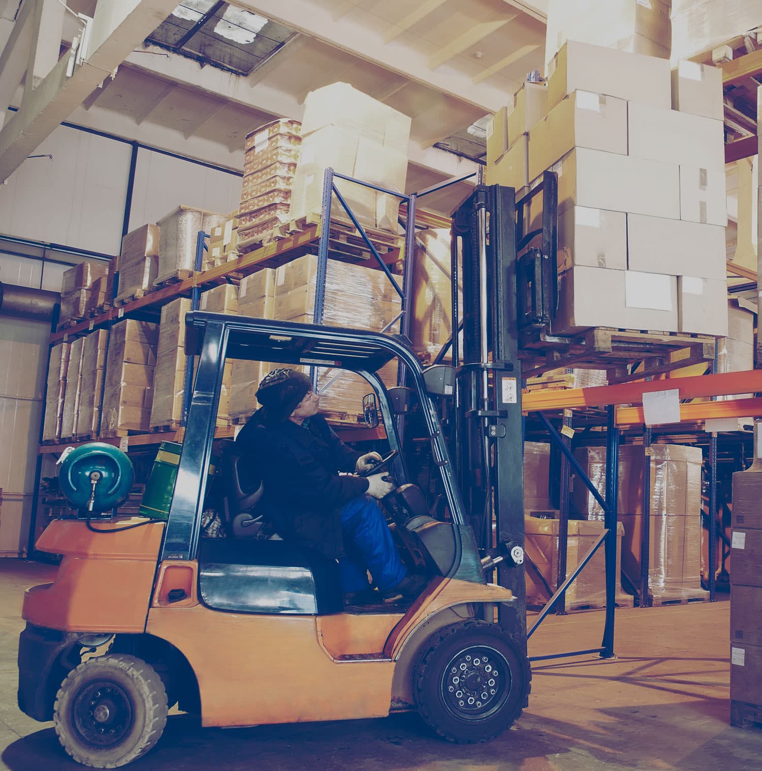 Man placing a skid of boxes on a storage shelf using a forklift. 