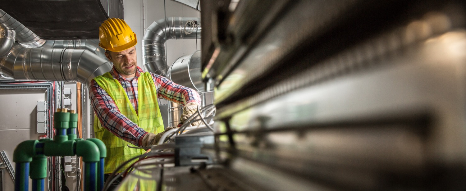 Construction worker making an adjustment to equipment in a large industrial furnace room that uses propane heating. 