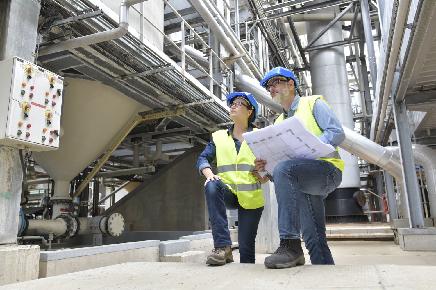 Two safety inspectors reviewing blueprints in a large industrial facility. 