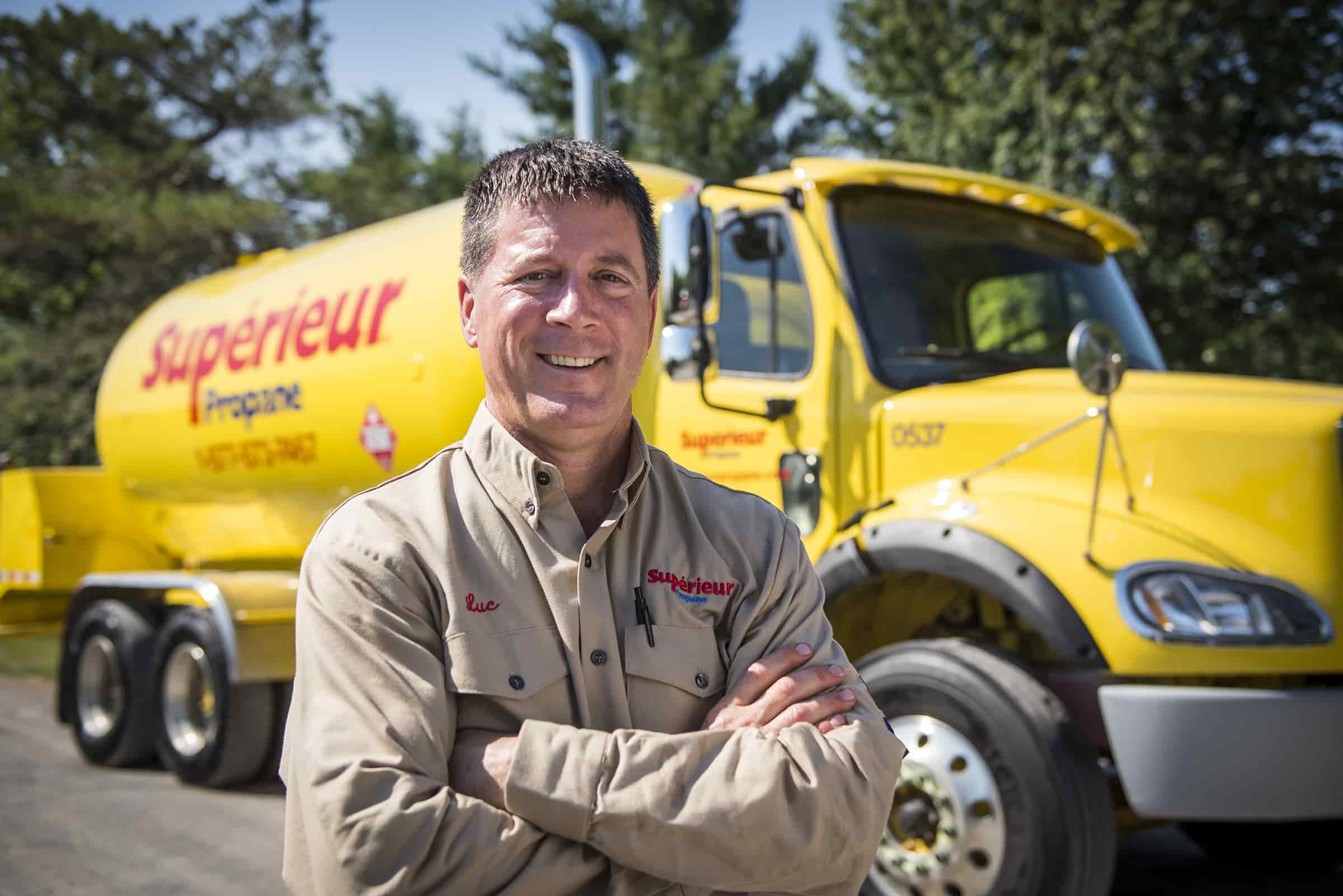 Cheerful Superior Propane driver stands in front of yellow truck.