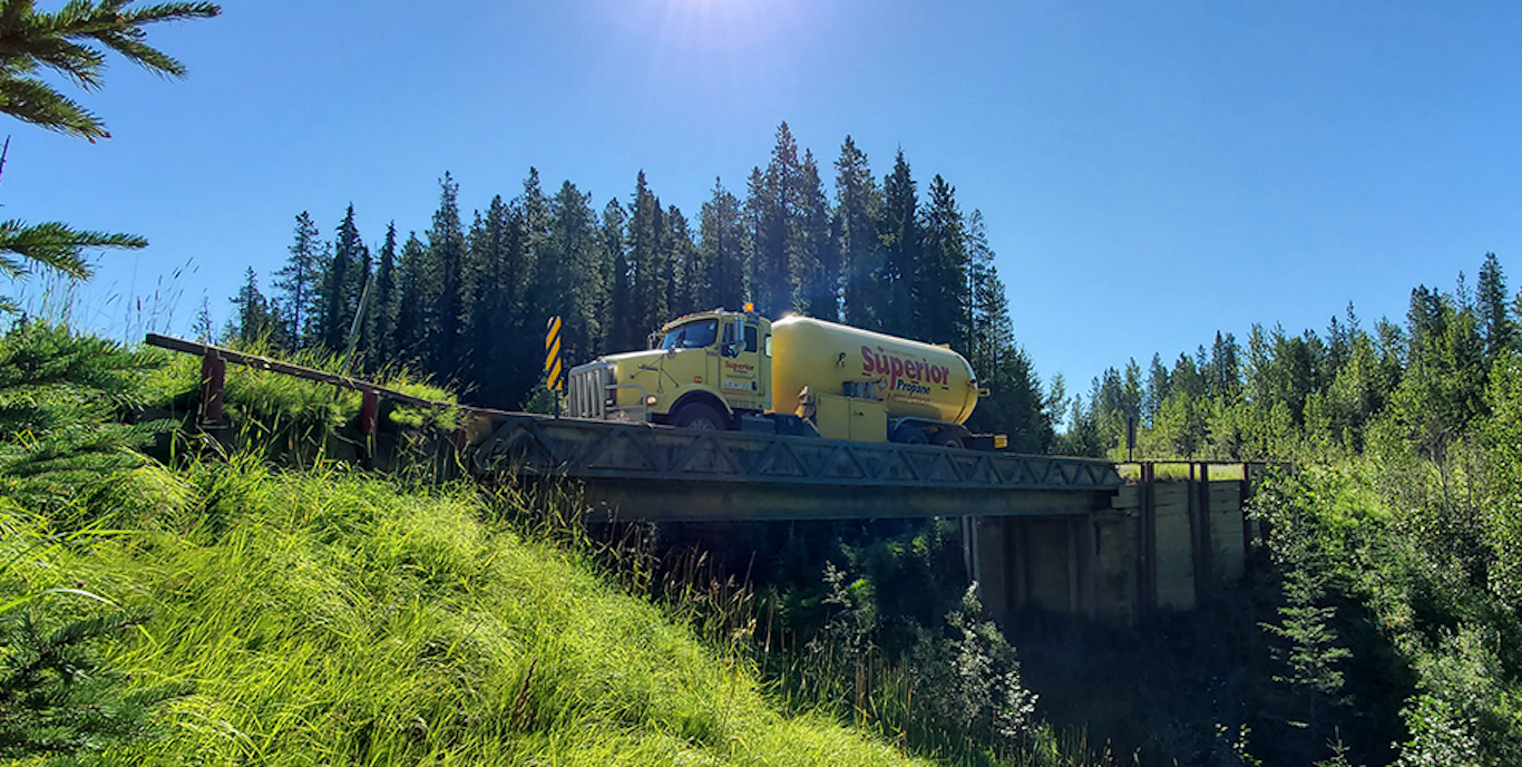 A Superior Propane truck on a bridge in front of a scenic background.